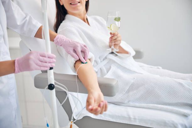 Person receiving IV drip, holding drink, in a medical setting.