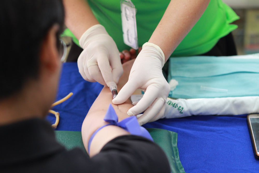 Person's arm being prepared for blood draw by a person wearing gloves in a medical setting.
