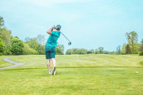 Golfer in teal shirt swings golf club on green, sunny course.