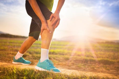 Person holding knee in pain while running outside. Sunny, outdoor setting.