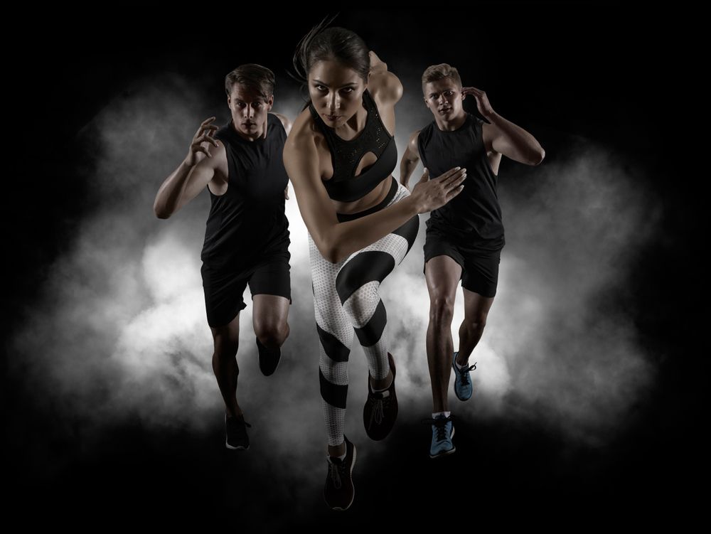 Three athletes sprinting toward the viewer against a black background with smoky effects.